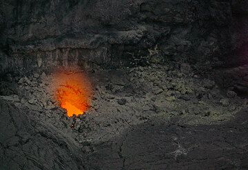 Un brillo débil de magma superficial es visible desde uno de los agujeros en el suelo de la fosa colapso. Mover magma es audible con chapoteando sonido ... (Photo: Tom Pfeiffer)