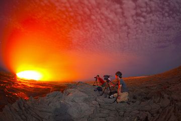 Two members from our group, Michel from Belgium and filmmaker Michael from Canada watching and photographing and filming the lava lake. The scene taken in extreme wide angle is illuminated by the strong glow from the lava and the light of the moon. (Photo: Tom Pfeiffer)