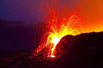 Explodierende Lava bricht aus dem Lavasee des Vulkans Erta Ale aus, gesehen in der Morgendämmerung. Lava wird geschleudert und durch eine Lücke in der Wand, in der sich der Lavasee befindet, nach draußen gedrückt. (Photo: Tom Pfeiffer)