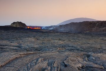 Weitwinkelaufnahme über die Caldera mit dem Lavasee in der Mitte vor einem kleinen Schlackenkegel und der westlichen Calderawand; Im fernen Hintergrund ragt ein weiterer Vulkan über der Szene auf. (Photo: Tom Pfeiffer)