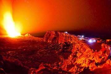 Group of people at the camp on the caldera rim watching the lava lake illuminate the caldera at night with bright red glow. (Photo: Tom Pfeiffer)