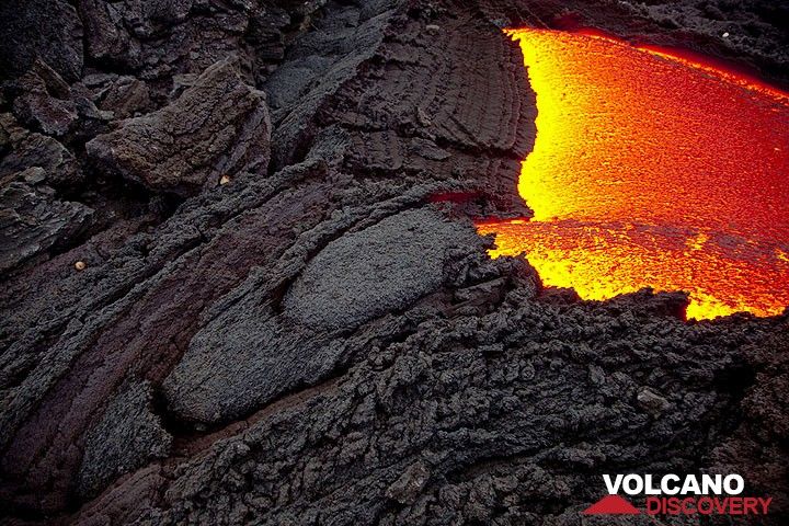 The lava flow emerging from its tube. Caused by friction and the sudden contact with cold air, successive segments of crust form at the exit, resulting in a progressive downstream growth of the tube's roof. (Photo: Tom Pfeiffer)