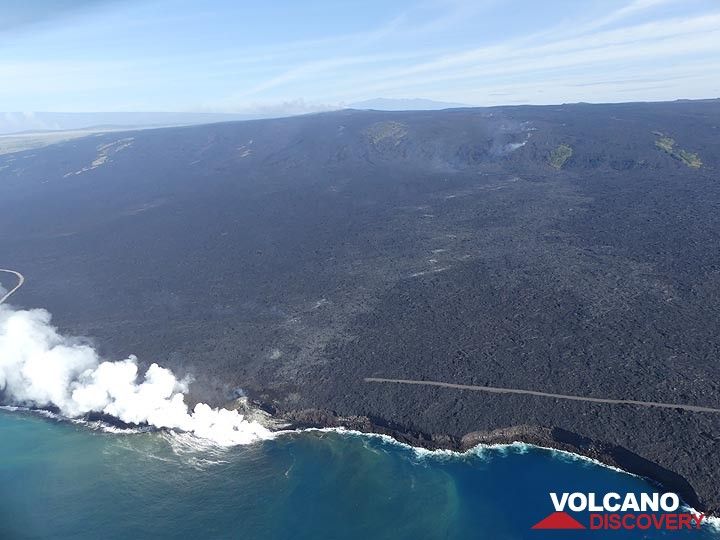 Extension day 3: Aerial overview of the Kamukona lava ocean entry, with the asphalt road destroyed by earlier lava flows, the steam trail marking the lava´s underground path and the steam cloud marking the Pu´u O´o lava shield and active crater in the central background (Photo: Ingrid Smet)