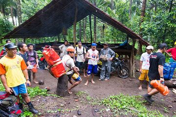 The strenuous, 5-6 hours hike up to Ibu's crater starts in a vast coconut palm plantation at the feet of the volcano. Porters gather and with the group and inspect luggage. (Photo: Tom Pfeiffer)