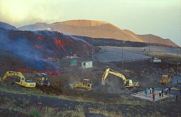 Der Lavastrom überquert gemächlich die Straße und verschlingt den Parkplatz. Bulldozer verstärken den Damm, der die Hauptgeäude auf dieser Seite schützen soll. (Photo: Tom Pfeiffer)