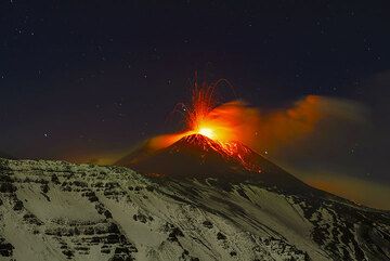 Tall strombolian explosion at the New SE crater and the snow-covered eastern headwall of the Valle del Bove in moonlight. (Photo: Tom Pfeiffer)