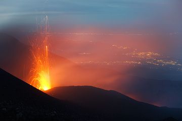 Strombolian eruption from the active vent on the May 13 fissure. Lights of Giarre, Taormina and the Strait of Messina in the background. (Photo: Tom Pfeiffer)