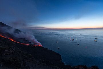 Tourist boats gather to see the spectacle from the sea as night falls. (Photo: Tom Pfeiffer)