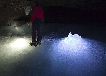 Rosario con sus grampones parado sobre el hielo dentro de la cueva. Mi linterna ilumina un montículo de hielo formado por gotas de agua helada del techo. (Photo: Tom Pfeiffer)