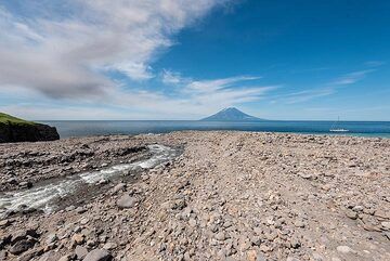 The mouth of the creek forms a vast pebble beach. The ash plume from the eruption in the previous picture is seen drifting NW towards Alaid. (Photo: Tom Pfeiffer)