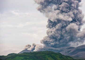 Ebeko-Ausbruch mittags von der Stadt Sewero-Kurilsk aus gesehen; Beachten Sie eine untere Aschewolke, die nach links wandert, während sich ein kleiner pyroklastischer Strom bildet. (Photo: Tom Pfeiffer)