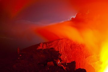 Nyiragongo-Vulkan bei Nacht: Gilles in seiner Lieblingsposition und beobachtet stundenlang die faszinierenden Bewegungen des Lavasees in der Nacht. Ganz links sind die Lichter von Goma zu sehen. (Photo: Tom Pfeiffer)