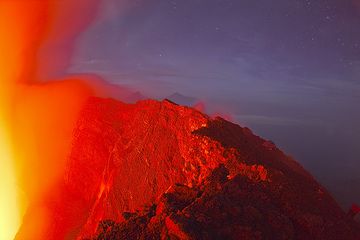 Mikeno y Karisimbi al fondo detrás de la pared iluminada del cráter del Nyiragongo. (Photo: Tom Pfeiffer)