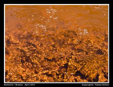 Gasblasen steigen von den Fumarolen in der Bucht auf Palea Kameni auf und wärmen das heilkräftige Meerwasser auf. Der rote Schlamm besteht aus Pyrit (FeS). (Photo: Tobias Schorr)