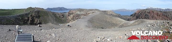 Panoramic view of the central area of Nea Kameni with eruption and explosion craters, monitoring equipment (front left) and a red-oxidised lava dome and flow (right). In the background one sees that caldera with (from left to right) the island of Therasia and the white villages of Oia and Fira on the island of Thera. (Photo: Ingrid Smet)