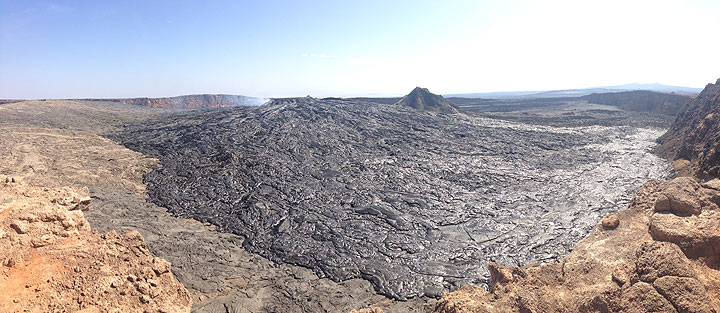 Panorama across Erta Ale´s caldera floor, clearly showing the large volume of fresh black shiny pahoehoe lavas that have recently overflowed from the lava lake which by now constructed its own containment rim (central-left in the background, where the gas plume rises from). (Photo: Hans and Jooske)