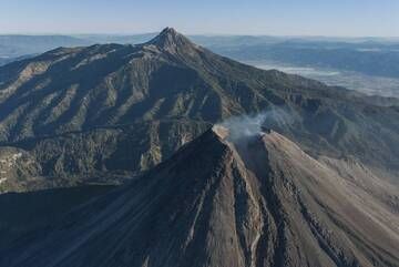 Nevado de Colima rises to an altitude of 4260 m in the background. Volcanic activity migrated progressively southward from Nevado de Colima in the Late Pleistocene to where the current Volcán de Colima edifice is located. The breach in the South side of the crater was produced as a consequence of the strong activity of Volcán de Colima which occurred in July 2015 and destroyed the previous summit lava dome. The picture was taken from a reconnaissance flight carried on January 15, 2016 looking to the North-East. (Photo: PepCabré)