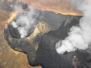 Aerial view of the central part of the Erta Ale's summit caldera with the north crater (left), south crater (right) and camp site on the caldera rim (centre below). Note the fresh black lava that spread all around the south crater and across the caldera floor in the lava lake overflowing event prior to the magma drainage and partially collapsing craters. (c)
