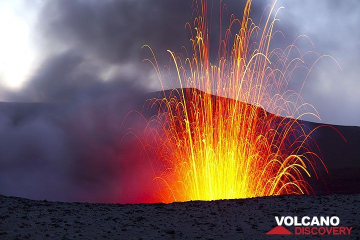 Wenn es dunkler wird, erlauben Langzeitbelichtungen, die parabolischen Flugbahnen der Bomben abzubilden, die mehr als 200 m über den Kraterrand hoch ausgeworfen werden. (Photo: Tom Pfeiffer)