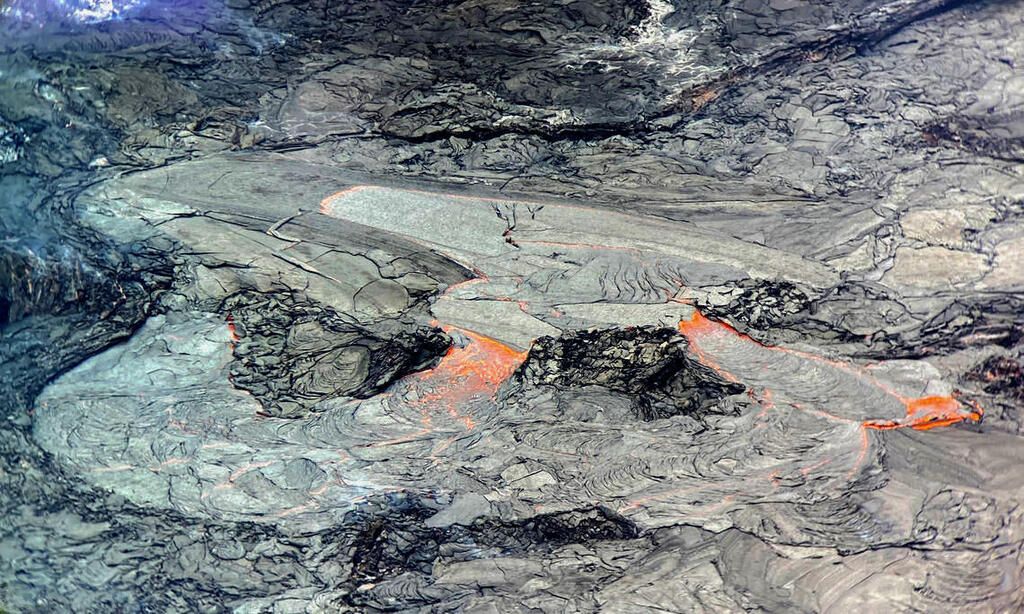 This close-up view of the active western portion of the Halema‘uma‘u lava lake at the summit of Kīlauea was captured on Thursday, May 6 through the lens of a laser rangefinder used by HVO scientists to measure distances to features within the crater. HVO scientists observed that the area immediately surrounding the inlet to the lava lake (above-center) was slightly perched relative to the rest of the active surface, and it was intermittently feeding lava channels to lower-lying parts of the lake (below-center and below-right). The western fissure is out-of-view to the upper-left and the main island in the lava lake is out-of-view to the right. USGS caption & image (color corrected).