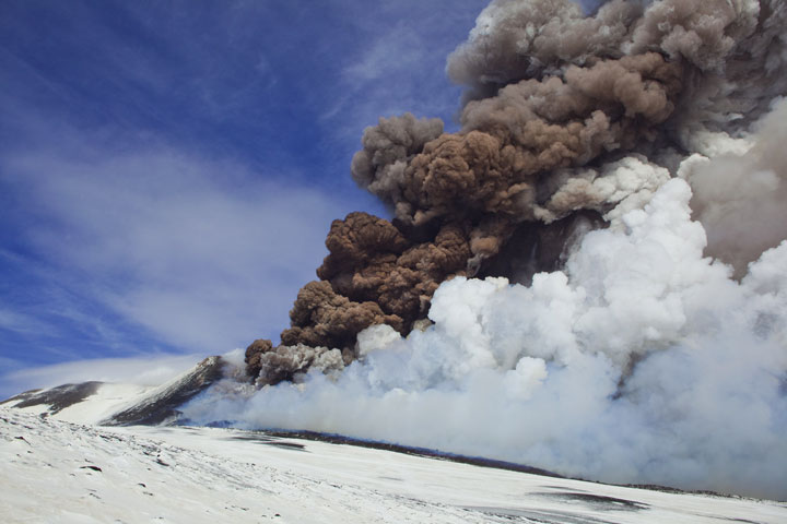 After having reached its peak, the eruption wanes quickly, but a dense brown ash plume still rises high from the fissure vent.