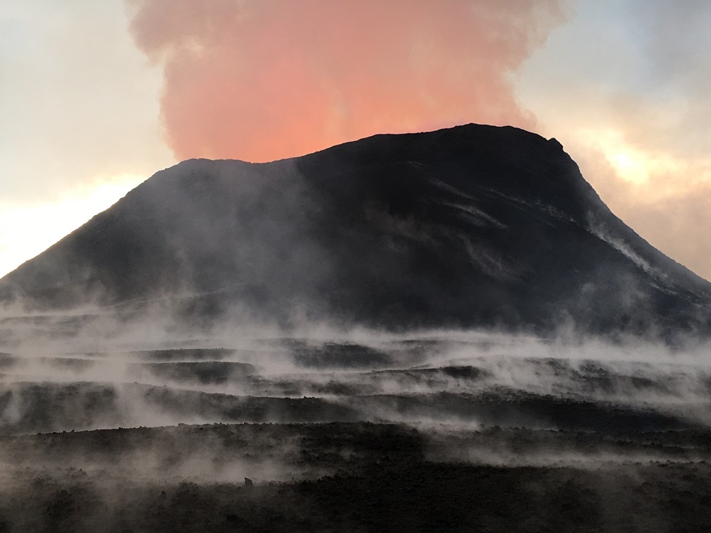 During the morning of June 16, 2018, the fissure 8 lava fountain was pulsing below the rim of the cinder cone that is now 51 m (170 ft) tall at its highest point. The steam in the foreground is the result of heavy morning rain falling on warm (not hot) tephra (lava fragments). (HVO/USGS)