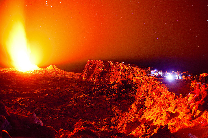 Strong nighttime glow of the active lava lake as seen from the caldera rim (bluish lights to the right are observers at Erta Ale camp site) (Dec 2010; image: Tom Pfeiffer)
